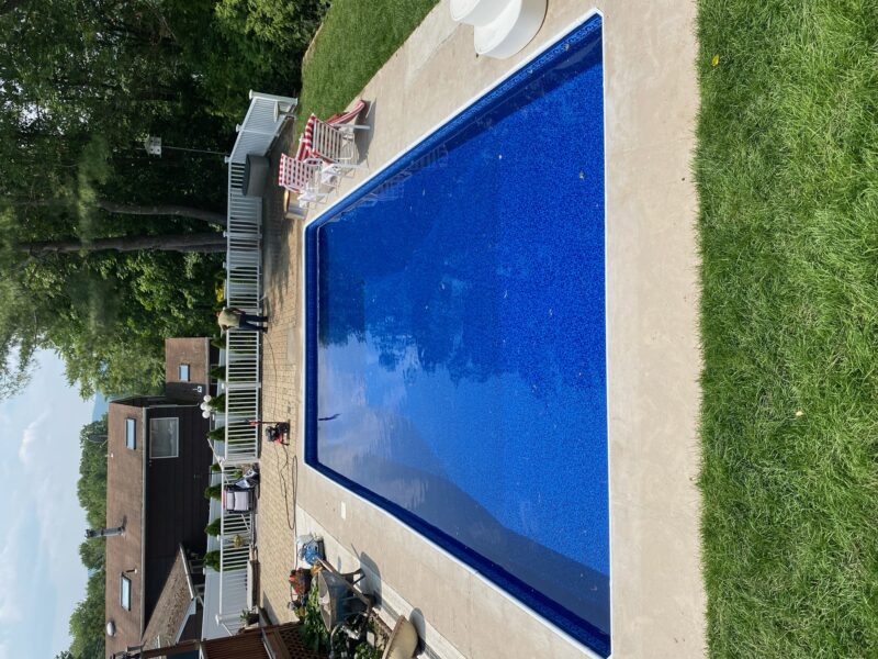 A picture of a square blue pool with a brown stone perimeter